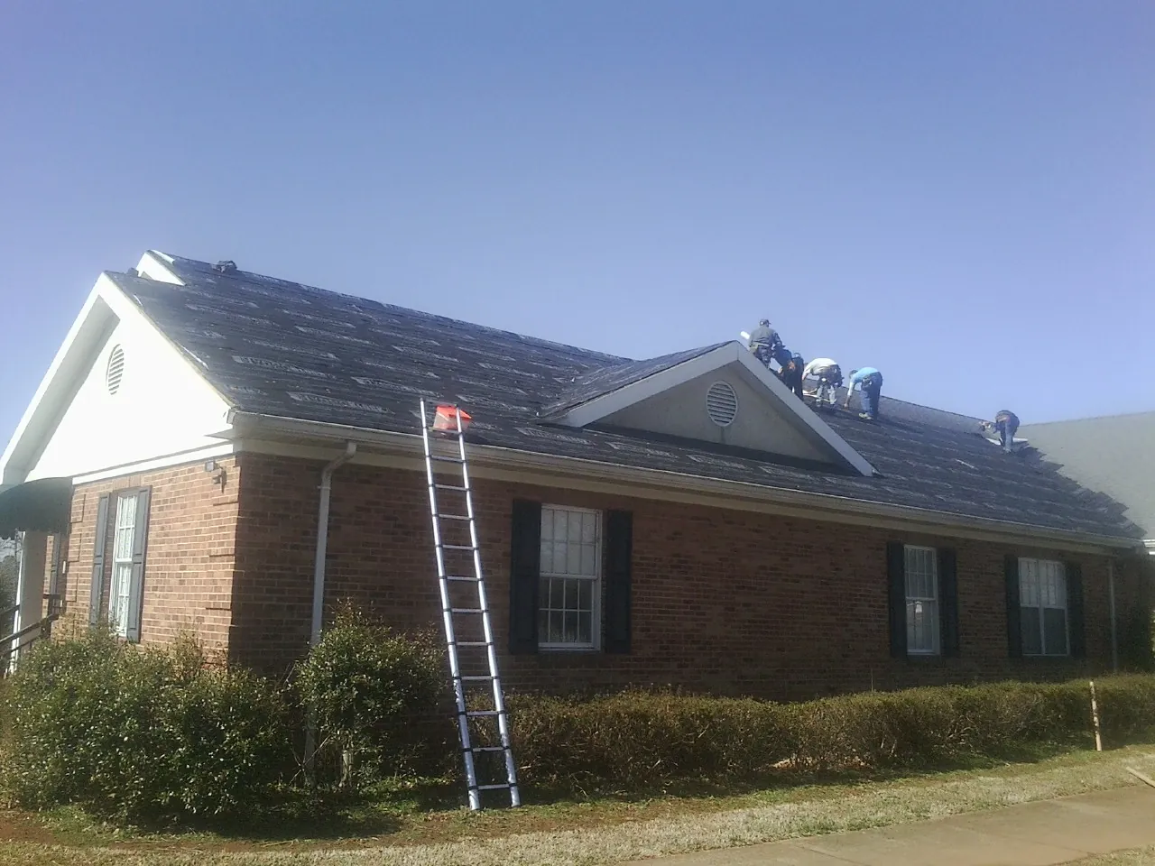 Crew tearing shingles off a brick ranch roof with a ladder set — Emergency Roof Repair work by our crew in Roseland