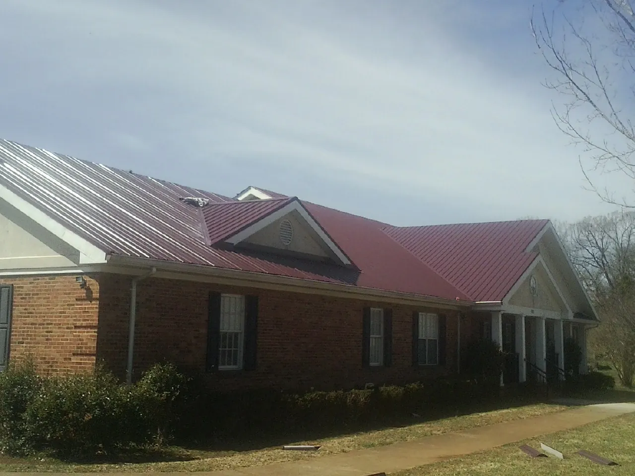 Red metal roof with gabled entries on a long brick building, from a Hail Damage Roof Repair job in Roseland