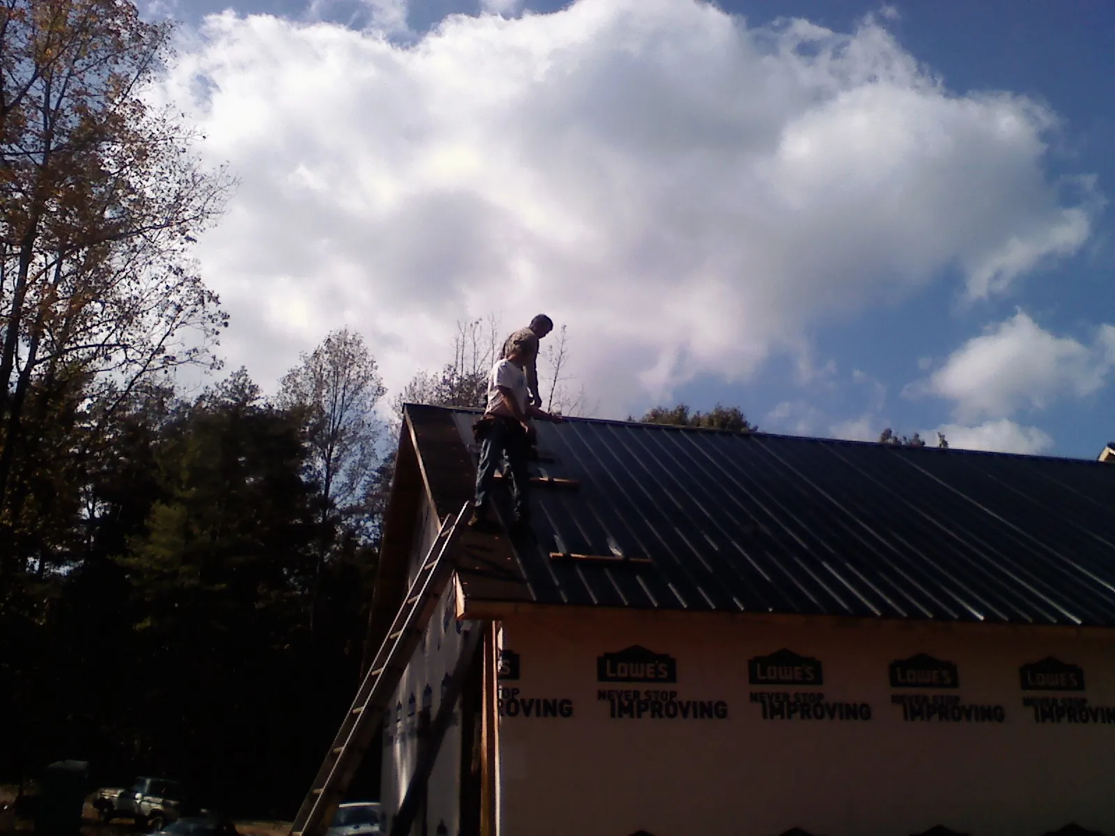 Roofer fastening dark metal panels high against a cloudy sky, from a Roof Inspection job in Roseland