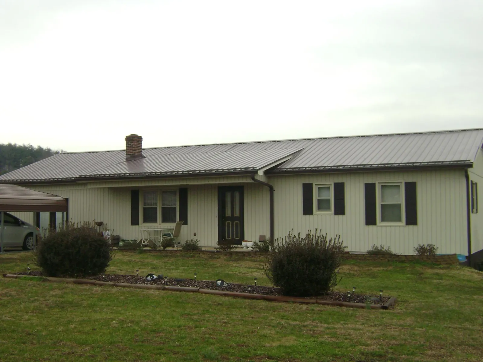 Brown metal roof on a cream sided ranch home with a brick chimney in Roseland