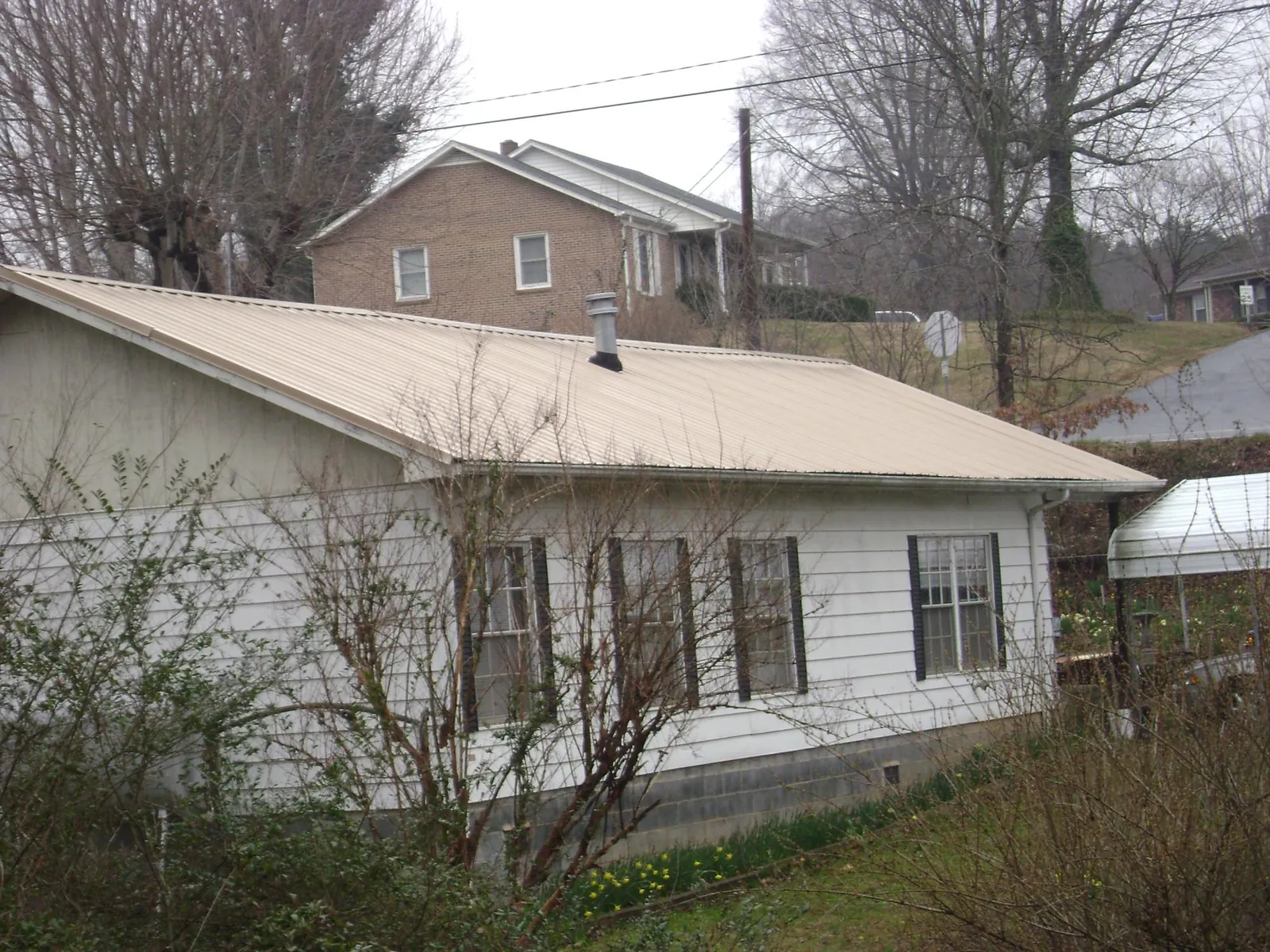 Tan metal roof on a white sided house set into a hillside — Commercial Roofing by Roofing Brothers in Roseland
